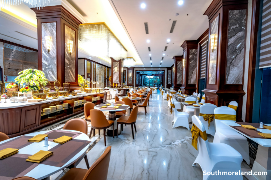 Elegant hotel dining room with buffet setup, marble floors, chandeliers, and arranged breakfast seating