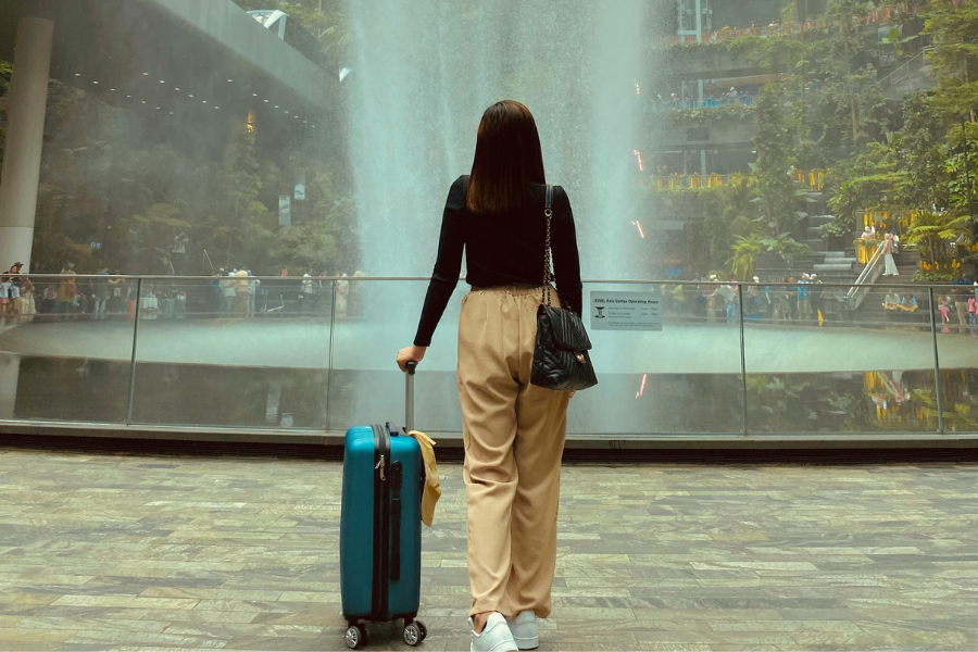 Solo female traveler with a suitcase viewing an indoor waterfall during her trip
